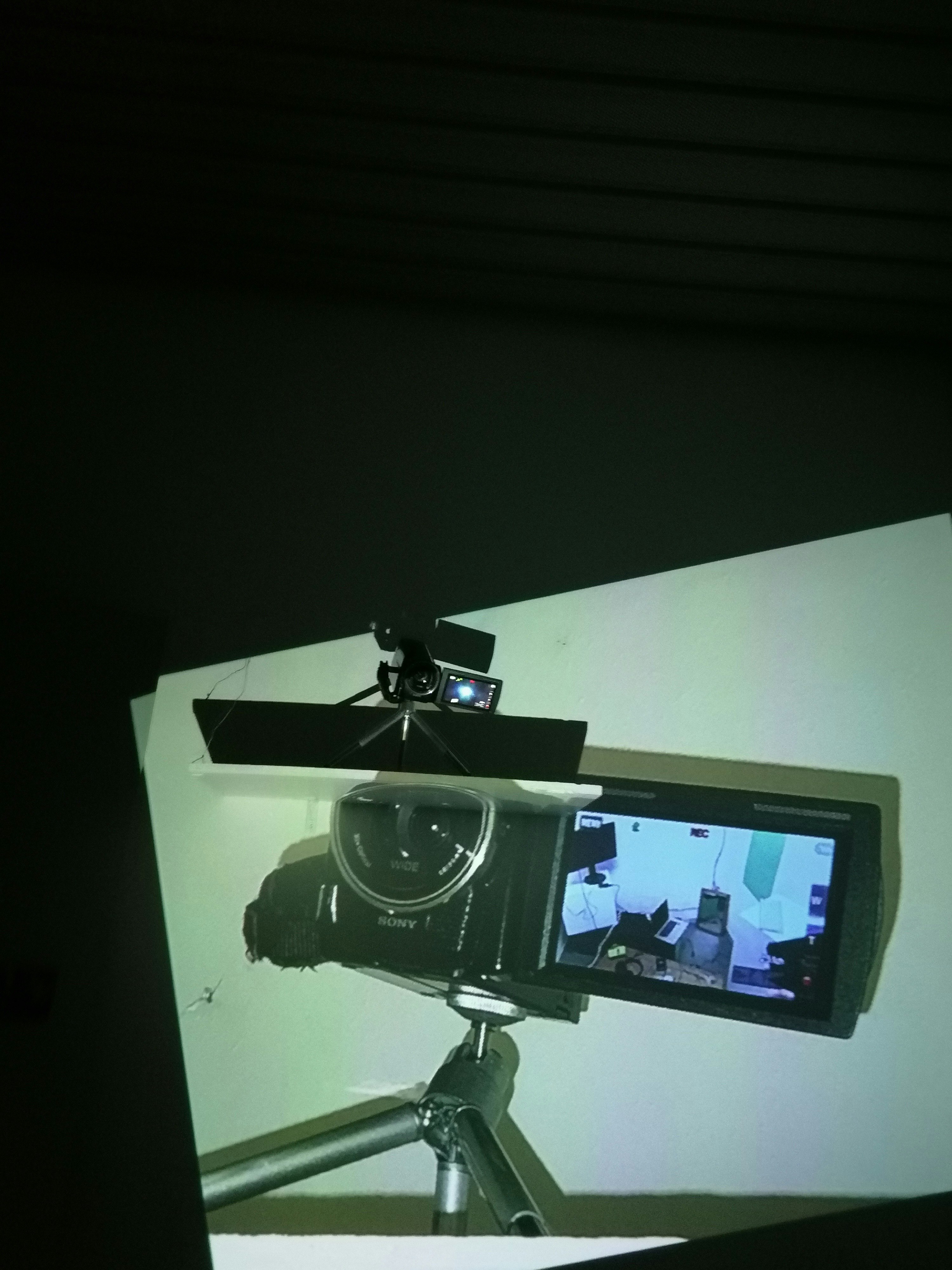 A high shelf with a handheld video camera, overlayed with a large projection of its image